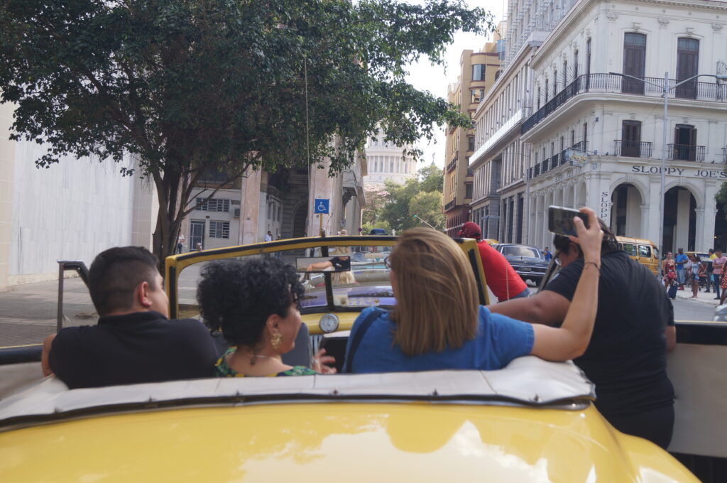 personas montadas en autos clásicos recorriendo La Habana